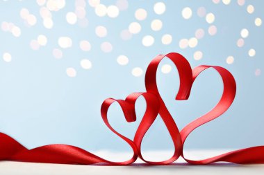 Mavi arka planda kırmızı kurdelelerden yapılmış iki kalp ve altın ışıklar.