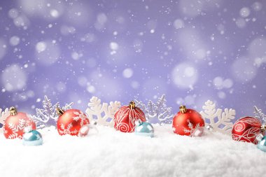 Mor arka planda kar taneleri olan kırmızı Noel topları