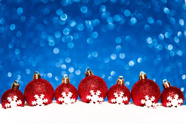 Bolas rojas de Navidad en la nieve sobre fondo de brillo azul — Foto de Stock