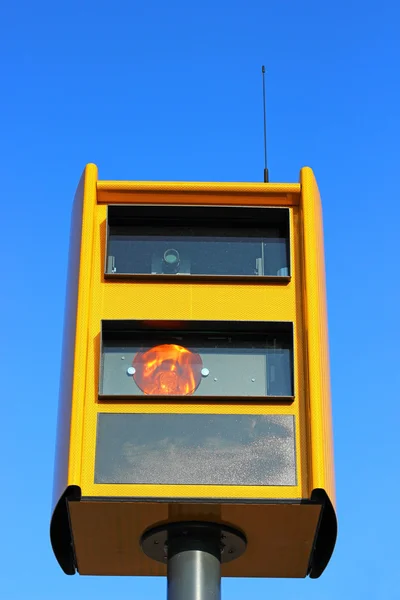 A traffic speed monitoring camera, against a bright blue sky.