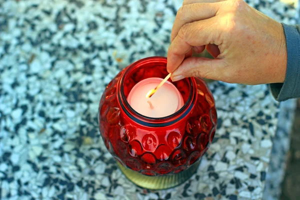 Woman at cemetery is lighting a red candle — Stock Photo, Image