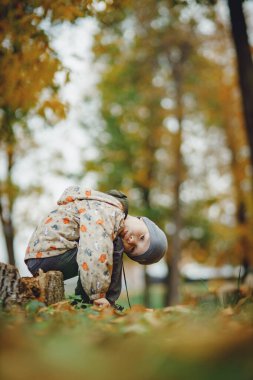 Sonbahar ormanında ağaç kütüğünde oturan çocuk.