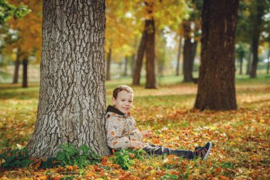 Sonbahar ormanında bir ağacın altında oturan çocuk.
