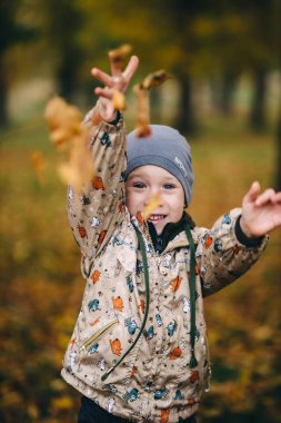 Çocuk parkta oynar, sonbahar yapraklarını fırlatır.