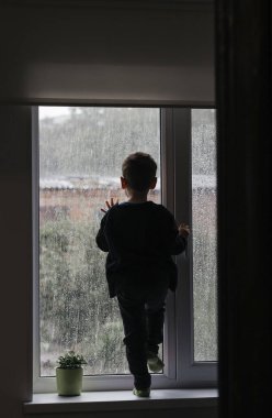 Çocuk pencereden dışarı bakar yağmura bakar.
