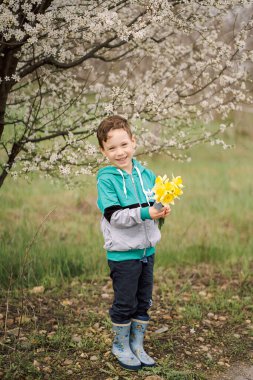 Çiçek açan bir ağacın altında nergis buketi olan bir çocuk.