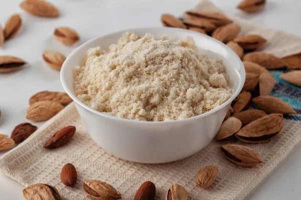 on a white table there are almond nuts and almond flour in a plate