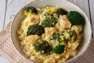 Tahta arka planda tavuk ve brokolili kremalı risotto.