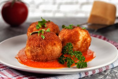 Lezzetli sıcak İtalyan arancini. Domates sosunda peynirle doldurulmuş pirinç topları. Eski ahşap bir masada bir tabakta.
