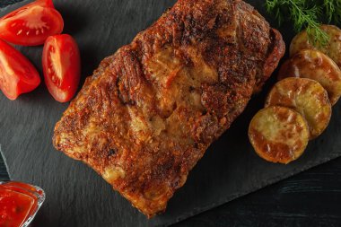 Izgara domuz pirzolası, domatesli grafit tahtasında servis edilir.