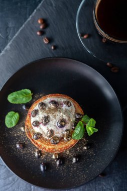 Ekşi krema ve taze böğürtlenli taze ev yapımı krepler, bir fincan kokulu kahveyle besin altınıyla süslenmiş.