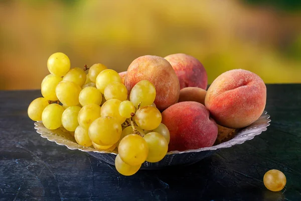 Ripe grapes and peaches in a metal bowl outdoors — Stock Photo, Image