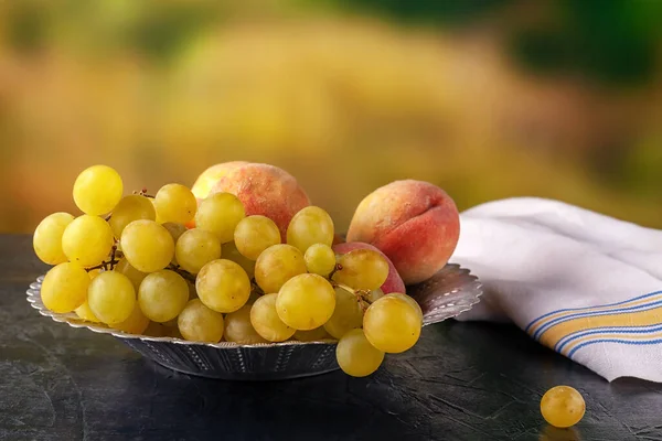 Ripe grapes and peaches in a metal bowl outdoors — Stock Photo, Image