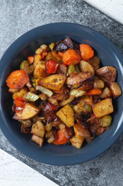 Koyu gri bir arkaplanda koyu mavi bir tabakta baharatlı haşlanmış sebzeler. Yukarıdan görüntüle.