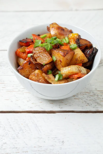 Diced cooked vegetables on light wood background in white plate. Healthy lunch - stewed garden vegetables. Traditional ratatouille with greens, zucchini, bell peppers and eggplant. Space for tex