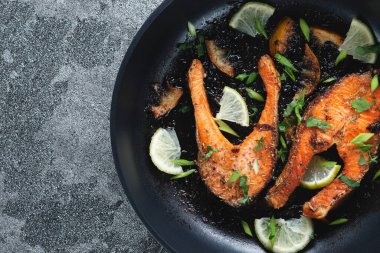 Limonlu, baharatlı ve limonlu ızgara somon bifteği ve kireç, kayrak taşı bir masada, yakın plan. Lezzetli pişmiş somon filetosu.