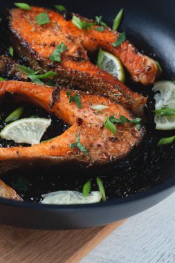 Limonlu, baharatlı ve limonlu ızgara somon bifteği. Hafif ahşap bir masada tavada. Lezzetli pişmiş somon filetosu.