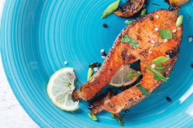 Mavi turkuaz balık tabağında limonlu, baharatlı ve limonlu ızgara somon bifteği. Lezzetli pişmiş somon filesi.