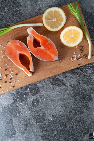 天然石のテーブルの上に玉ねぎ レモン スパイスを入れた木製のまな板の上で新鮮なサーモンステーキをジューシーに クローズアップ おいしい鮭フィレを調理 — ストック写真
