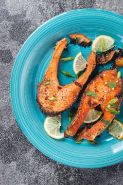 Sulu ızgara somon bifteği, limon, baharat ve limon, taş bir masa üzerinde mavi turkuaz balık tabağında. Lezzetli pişmiş somon filetosu.