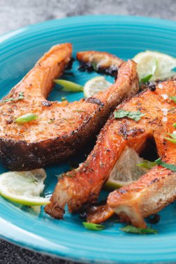 Sulu ızgara somon bifteği, limon, baharat ve limon, taş bir masa üzerinde mavi turkuaz balık tabağında. Lezzetli pişmiş somon filetosu.