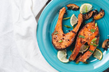 Sulu ızgara somon bifteği, limon, baharat ve limon, taş bir masa üzerinde mavi turkuaz balık tabağında. Lezzetli pişmiş somon filetosu.