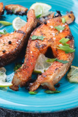 Sulu ızgara somon bifteği, limon, baharat ve limon, taş bir masa üzerinde mavi turkuaz balık tabağında. Lezzetli pişmiş somon filetosu.
