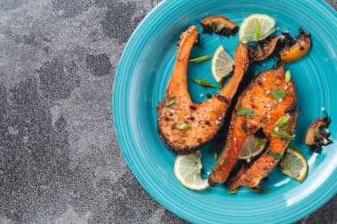 Sulu ızgara somon bifteği, limon, baharat ve limon, taş bir masa üzerinde mavi turkuaz balık tabağında. Lezzetli pişmiş somon filetosu.