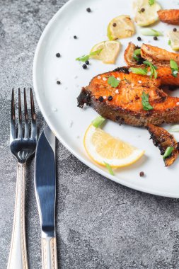 Limonlu ızgara somon bifteği, baharat ve kireç taş bir masada beyaz bir tabakta. Lezzetli pişmiş somon filesi.