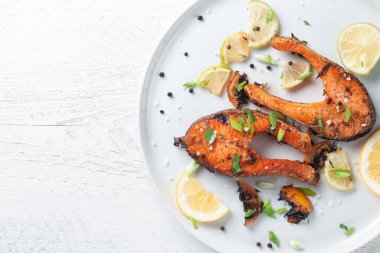 Limonlu ızgara somon bifteği, baharat ve limon beyaz bir tabakta, ahşap bir masada. Lezzetli pişmiş somon filesi.