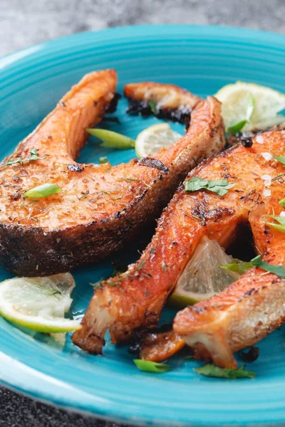 Sulu ızgara somon bifteği, limon, baharat ve limon, taş bir masa üzerinde mavi turkuaz balık tabağında. Lezzetli pişmiş somon filetosu.