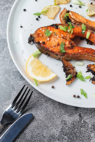 Limonlu ızgara somon bifteği, baharat ve kireç taş bir masada beyaz bir tabakta. Lezzetli pişmiş somon filesi.