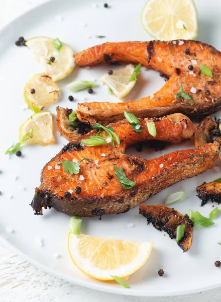 Limonlu ızgara somon bifteği, baharat ve limon beyaz bir tabakta, ahşap bir masada. Lezzetli pişmiş somon filesi.