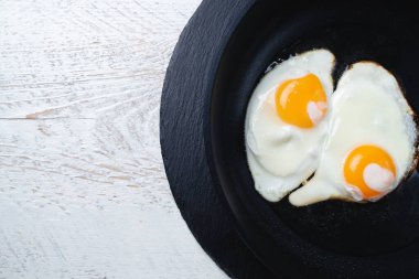 Hafif ahşap bir masada, siyah bir tavada kızarmış yumurta. Yakın plan, mesaj için yer. 