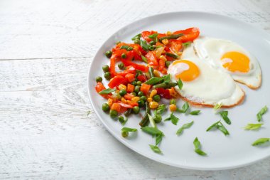 Kızarmış yumurta ve sebzeler beyaz bir tabakta.