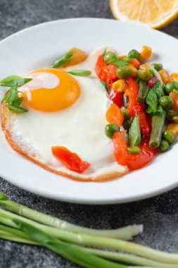 Kahvaltı için gri beton bir masada beyaz bir tabakta yumurta ve sebzeler, yakın plan.