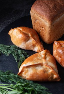 Taze pişmiş yiyecekler. Köfteli çavdar ekmeği ve koyu arkaplanda bir masa üzerindeki yeşillikler.