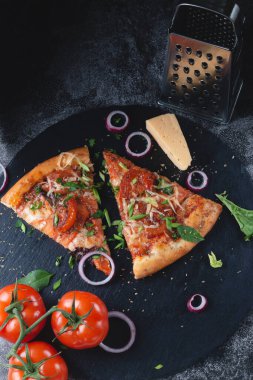 Geleneksel İtalyan biberli pizza domatesli, rendelenmiş metal peynirli, soğanlı ve otlu, siyah bir sırtüstü siyah bir masada.