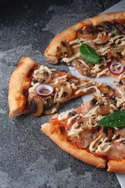 Ev yapımı İtalyan pizzası. Mantarlı, jambonlu, domatesli, peynirli, soğanlı ve otlu. Koyu bir taş masa üzerinde.