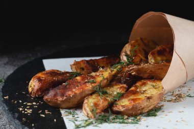 Kahverengi kraft ambalaj kağıdına sarılı lezzetli patates parçaları. Fast food servisi. Kırsal ahşap arka planda kızarmış patates. Taştaki patatesler. Kızarmış cips, patates dilimleri. Üst görünüm