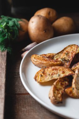 Baharatlı, dereotlu ve yeşil soğanlı büyük beyaz bir tabakta ahşap bir masada nefis pişmiş köy patatesleri.