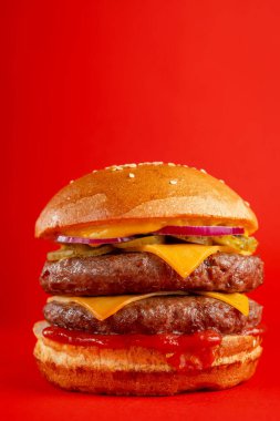 Kırmızı arka planda çift biftekli ve çedar peynirli lezzetli burger. Peynirli ve iki köfteli leziz sağlıksız burger. Fast food, sağlıksız gıda konsepti.