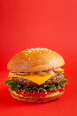 Kırmızı arka planda biftekli ve çedar peynirli lezzetli burger. Peynirli ve iki köfteli leziz sağlıksız burger. Fast food, sağlıksız gıda konsepti.