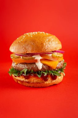 Kırmızı arka planda biftekli ve çedar peynirli lezzetli burger. Peynirli ve iki köfteli leziz sağlıksız burger. Fast food, sağlıksız gıda konsepti.