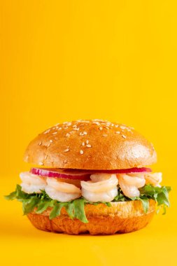 Karidesli lezzetli burger, sarı arka planda izole edilmiş. Lezzetli taze sağlıksız hamburgerler. Dikey pankart 
