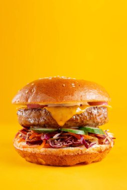 Sarı arka planda izole edilmiş lezzetli bir burger. Peynirli lezzetli ve sağlıksız hamburgerler. Dikey pankart 
