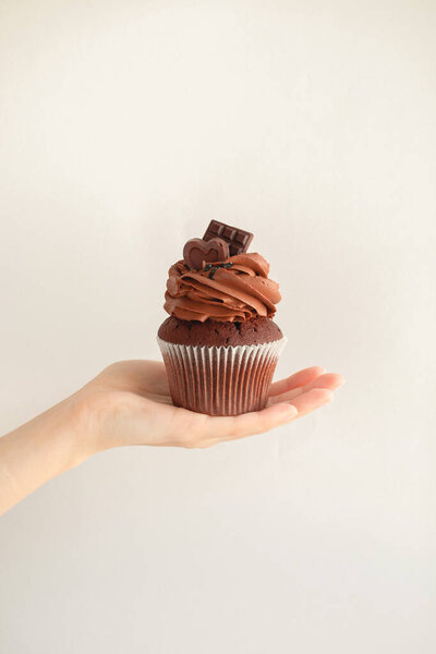 Girl's hand holds a brown chocolate cupcake on a neutral gray background