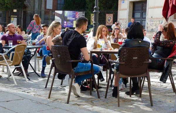 Madrid, İspanya - 1 Nisan 2021: Latin Mahallesi 'ndeki açık terasta bir grup genç oturuyor. Maskesi olmayan erkek ve kadınlar salgın sırasında şehir sokaklarında içki içiyorlar.