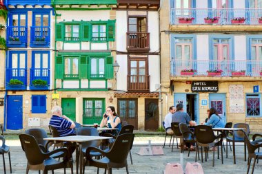Hondarribia, Bask bölgesi, İspanya - 8 Temmuz 2021: farklı yaşlarda insanlar siesta saatlerinde yerel barın terasında dinleniyorlar. Arka planda eski şehrin canlı renkli binaları