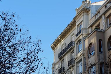 Çarpıcı tarihi bir binada eşsiz mimari ayrıntılar, balkonlar ve sıcak renkler bulunur. Açık mavi gökyüzü sahnenin cazibesini artırıyor. Birkaç yapraksız ağaç manzarayı çerçeveliyor..